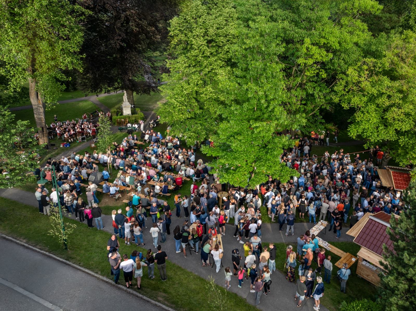 Luftaufnahme: Viele Menschen feiern gemeinsam im Park, im Hintergrund spielt die Musikkapelle